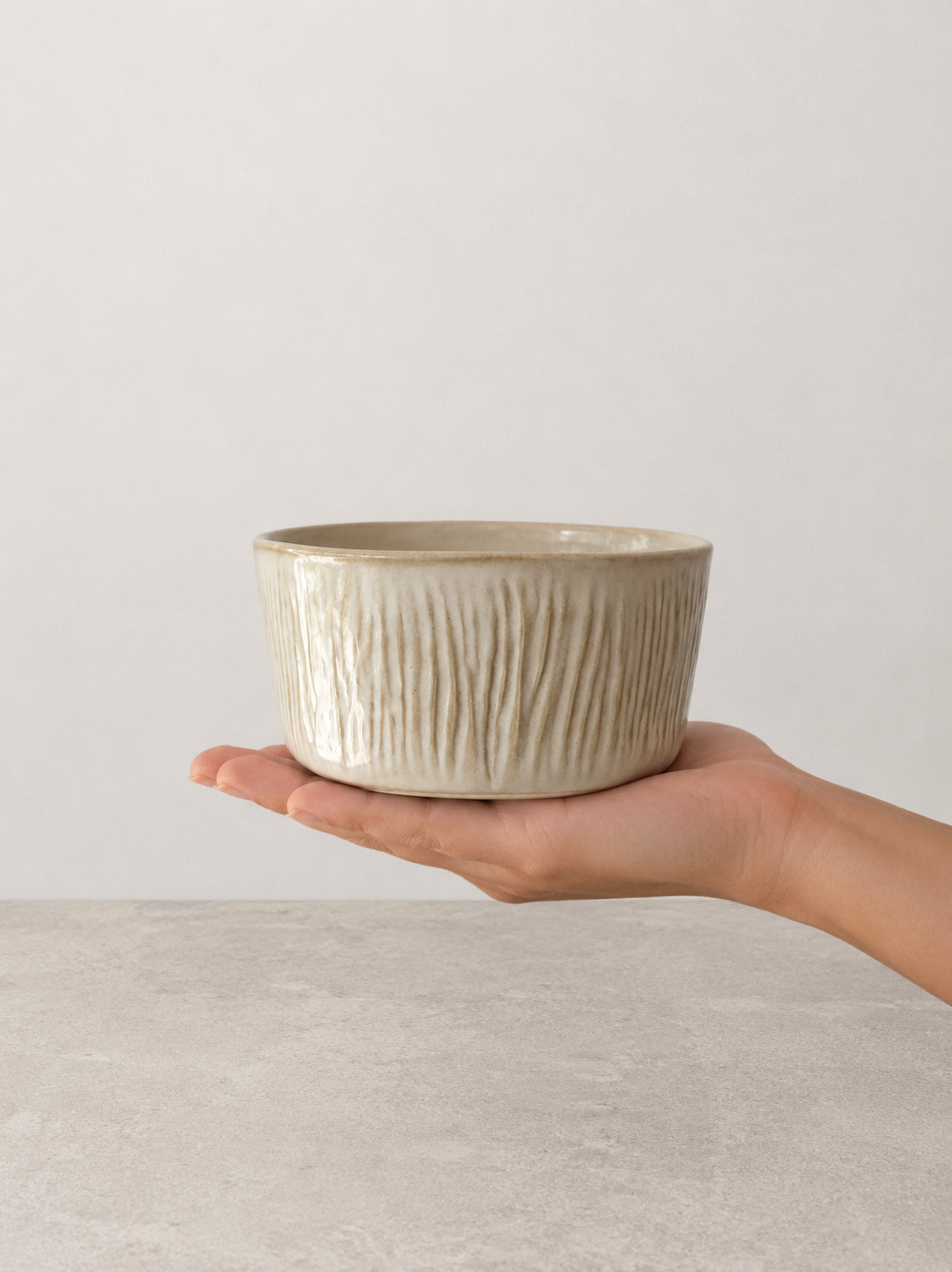 Creme stoneware bowl by SOLI CERAMICS held in hand against a neutral background