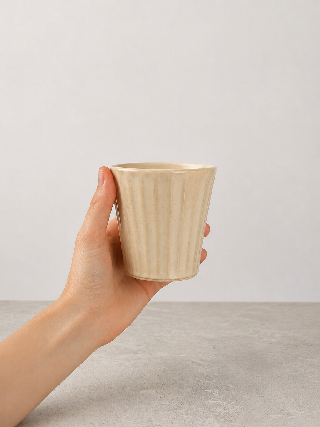Creme stoneware mug by SOLI CERAMICS held in hand against a neutral background