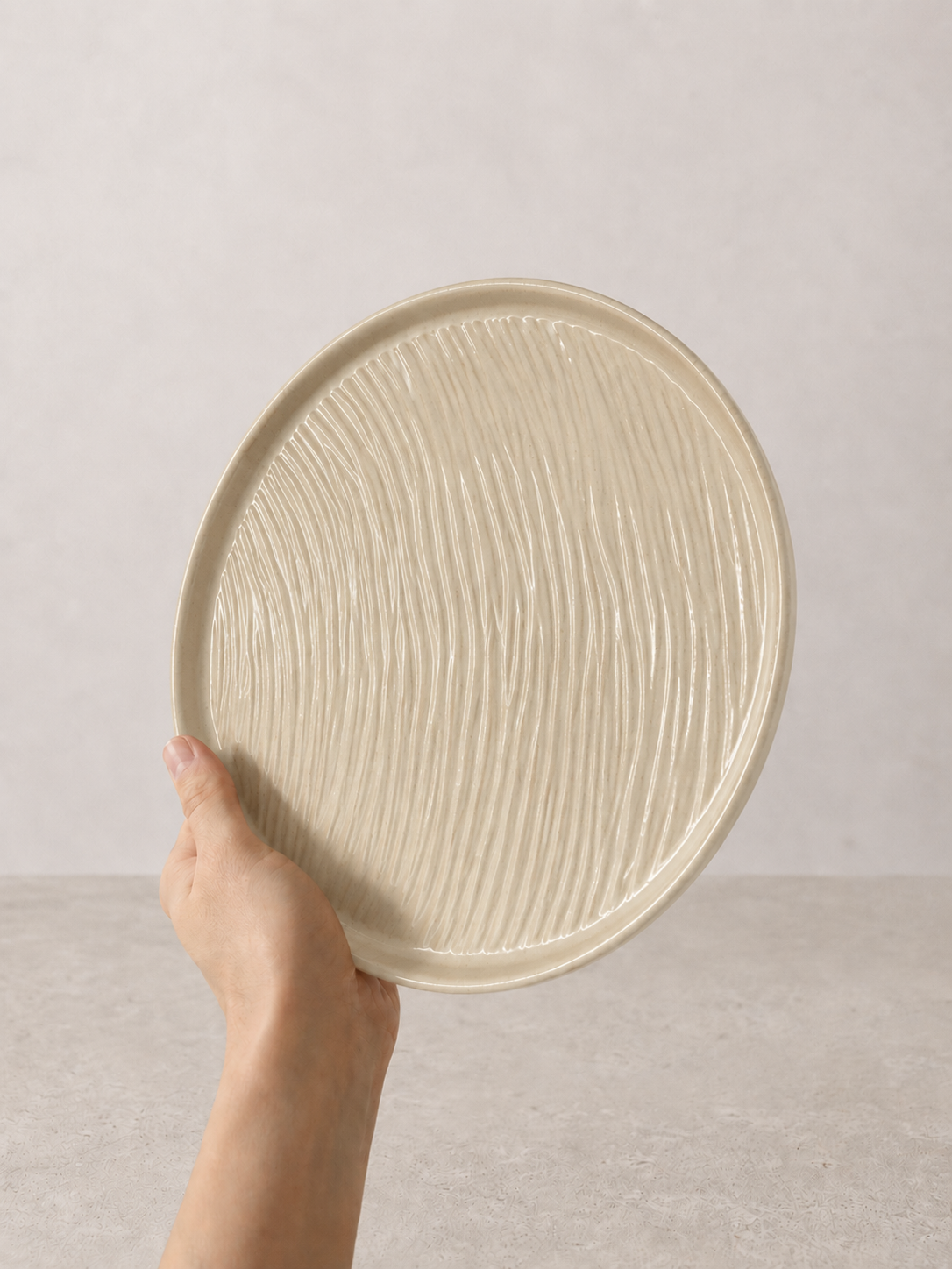 Creme stoneware plate by SOLI CERAMICS held in hand against a neutral background