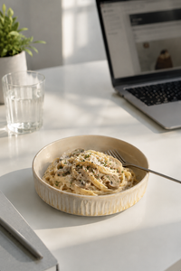 Creme stoneware salad/pasta plate with creamy mushroom pasta on a white desk